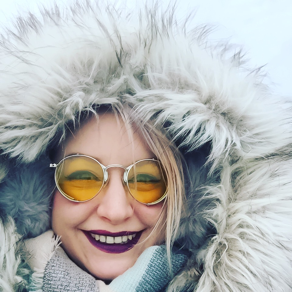Close-up of Ms. Unexpected's face with a faux-fur hood, earmuffs, a scarf, and sunglasses.